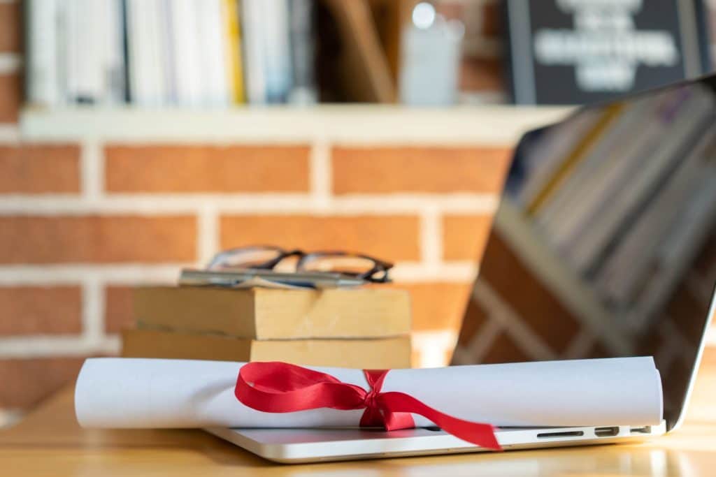 Close up of a graduation diploma laying on top of an open keyboard next to a stack of books.